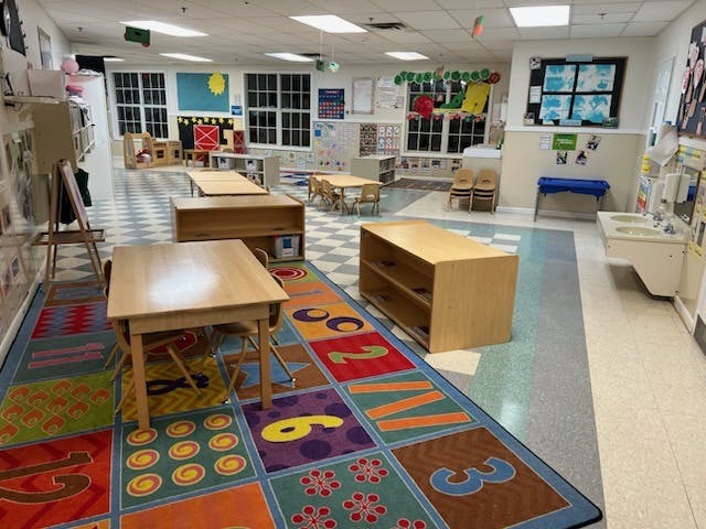 Classroom with small wooden tables and chairs, and a colorful rug