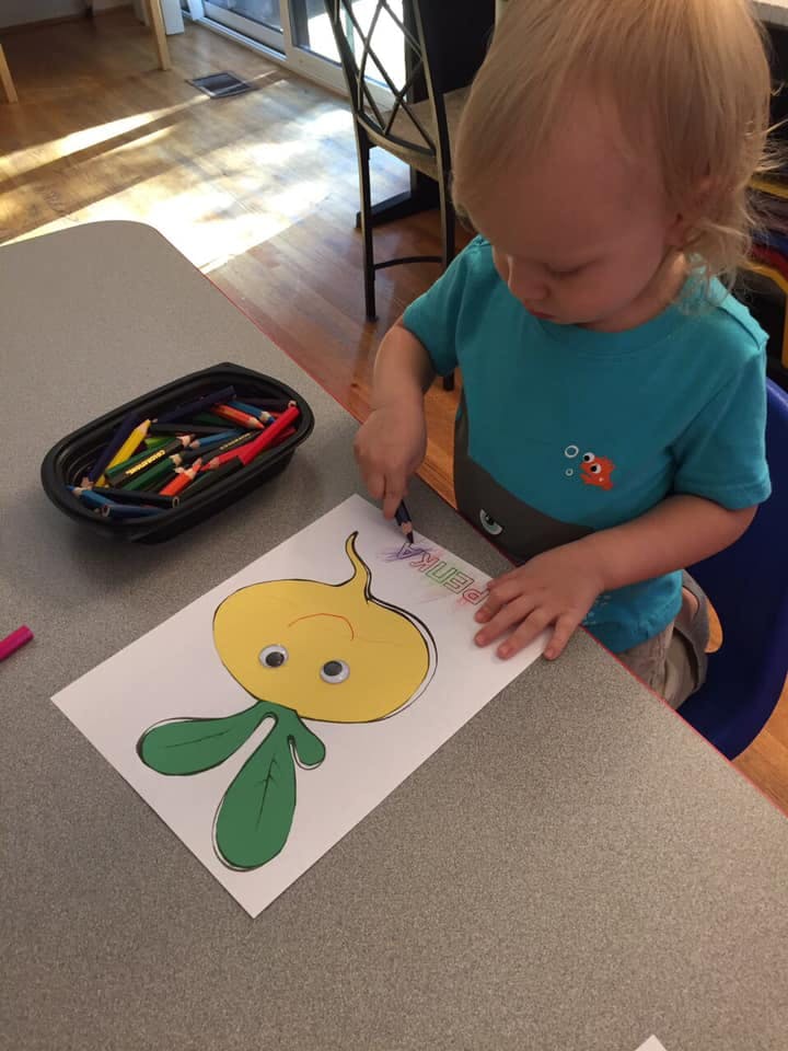 Child coloring a cartoon character on paper at a table