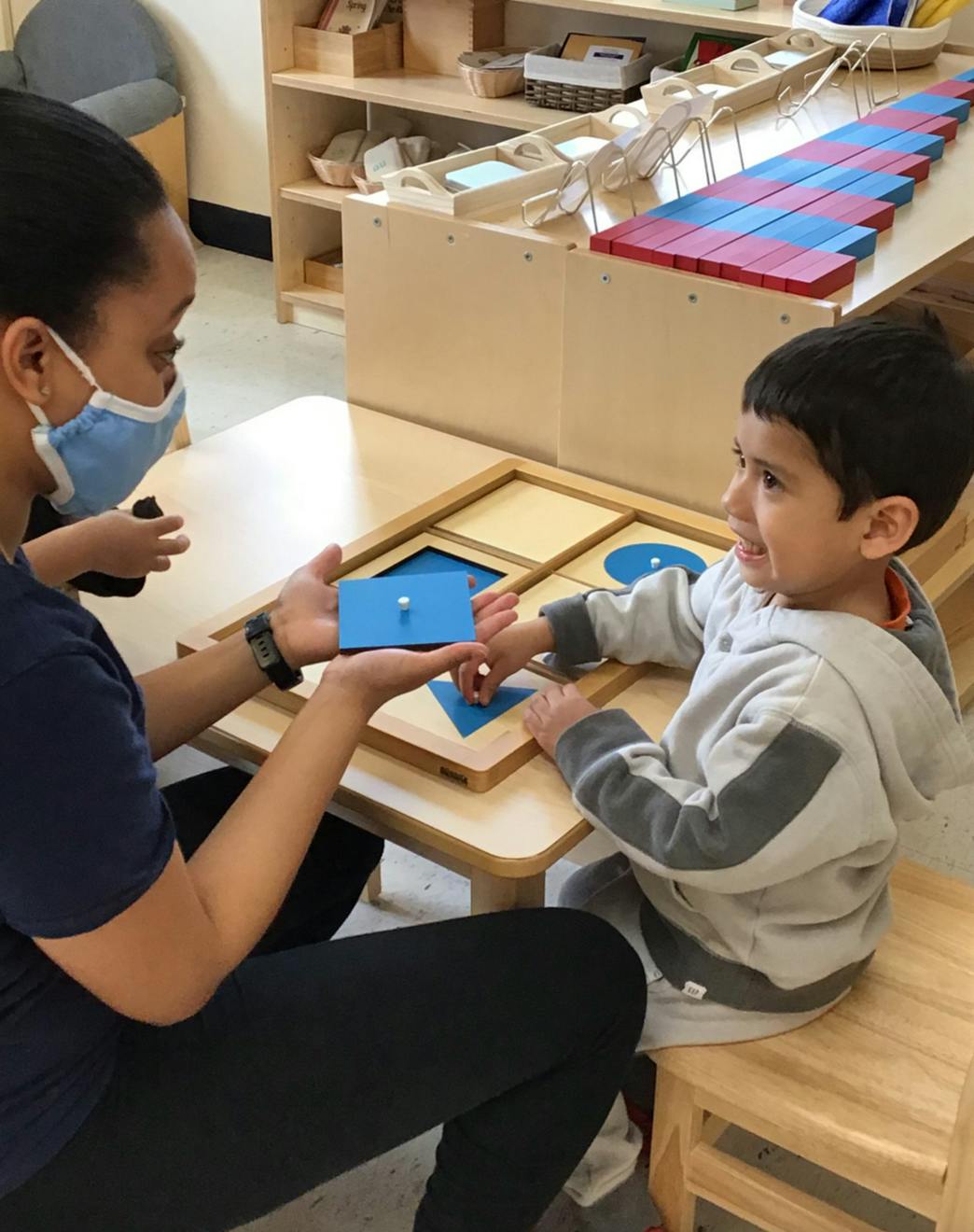 Person in mask and child playing with shape puzzle