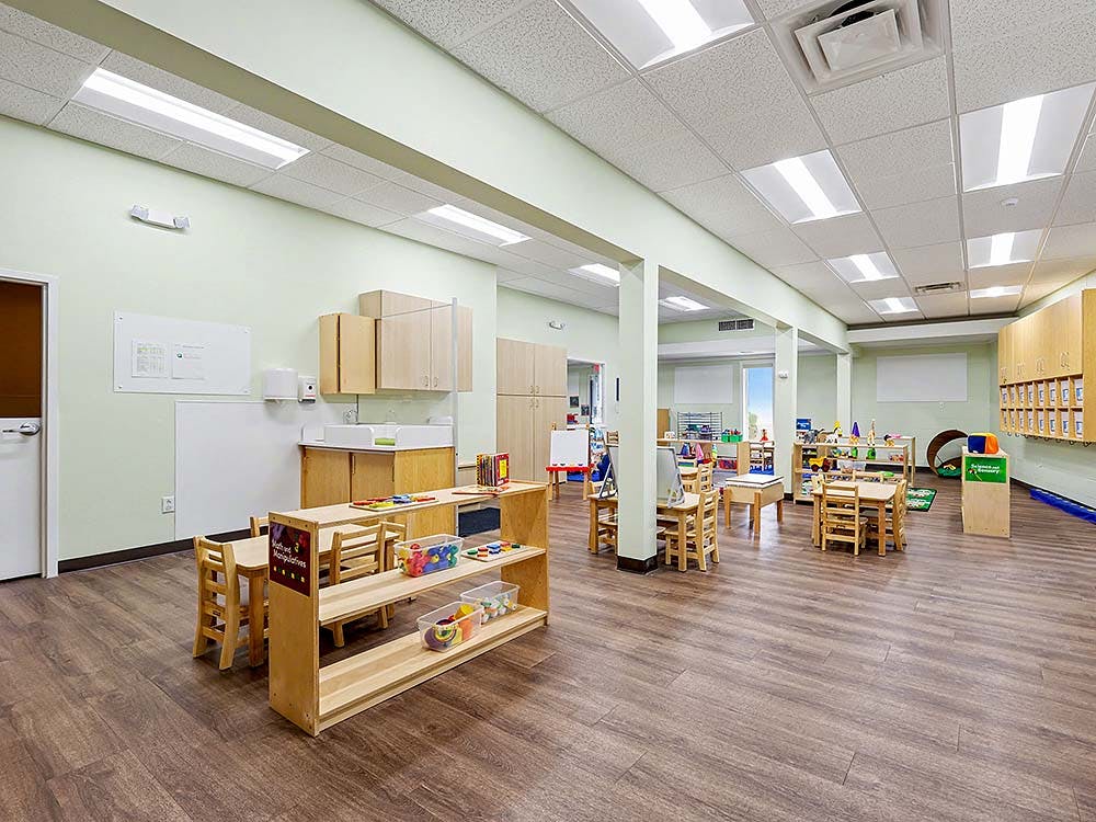 Empty classroom with small wooden tables, chairs, and shelving units