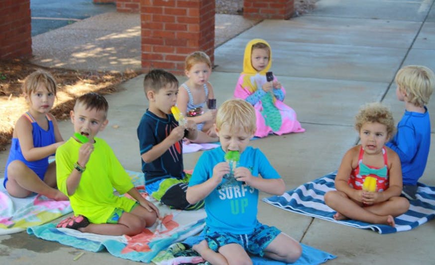 Children sitting on towels eating popsicles