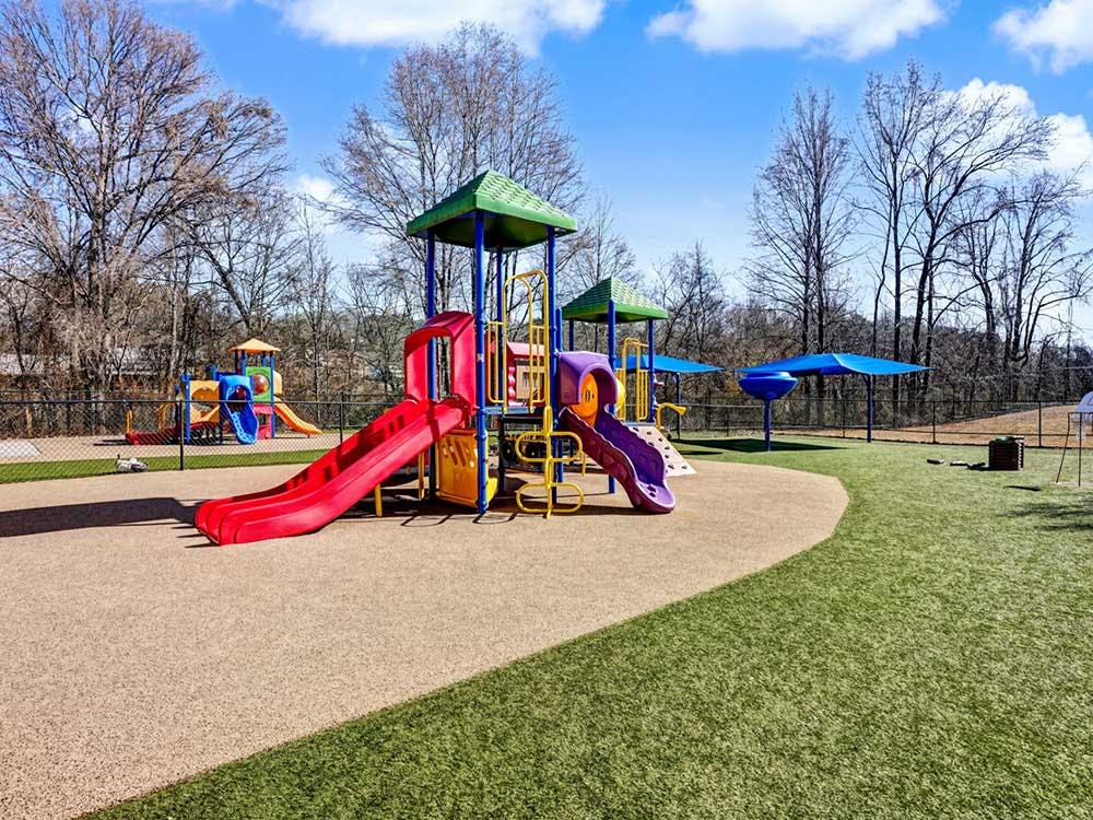 Colorful playground structures with slides on a soft surface surrounded by grass