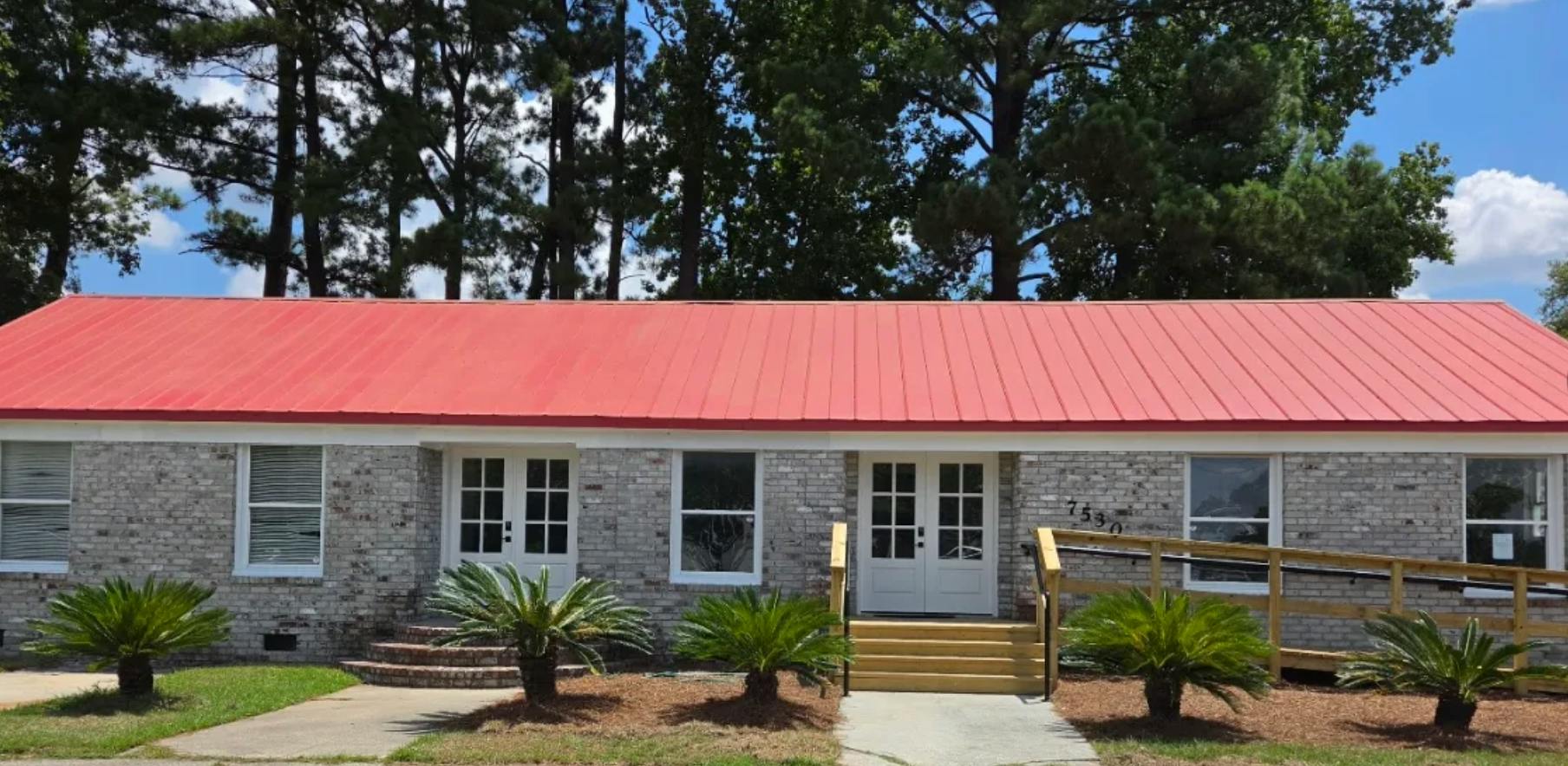 Single story brick building with a red metal roof and two entry doors