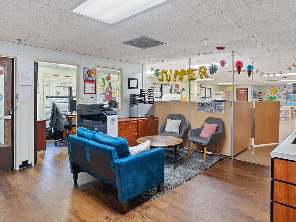 Lounge area in an office with a blue couch, chairs, and office equipment
