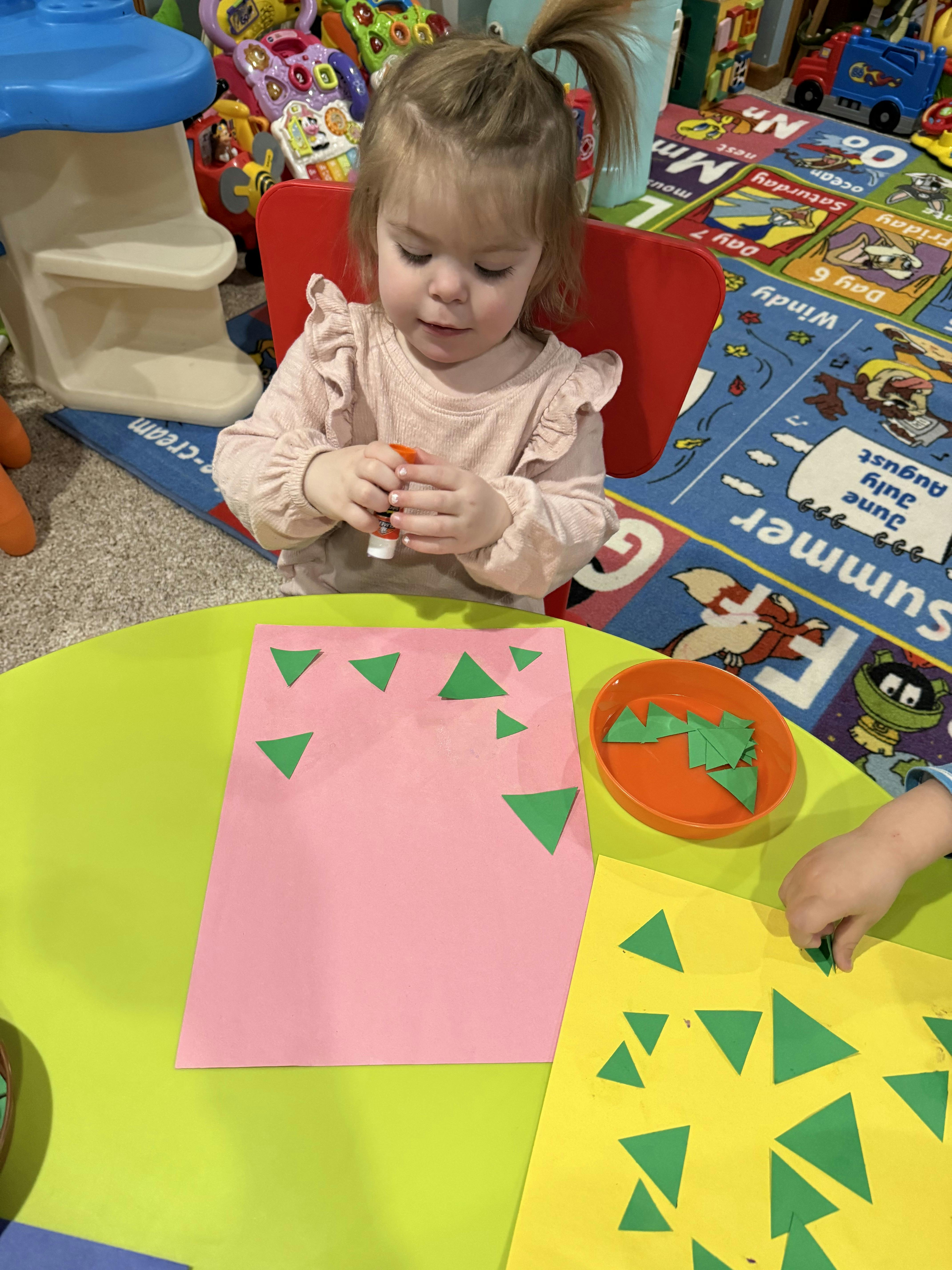 Child gluing green paper triangles onto pink paper