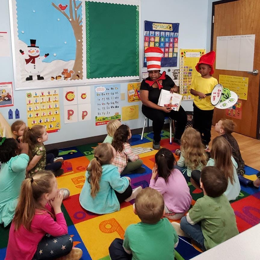 Person in striped hat reading to children in a classroom