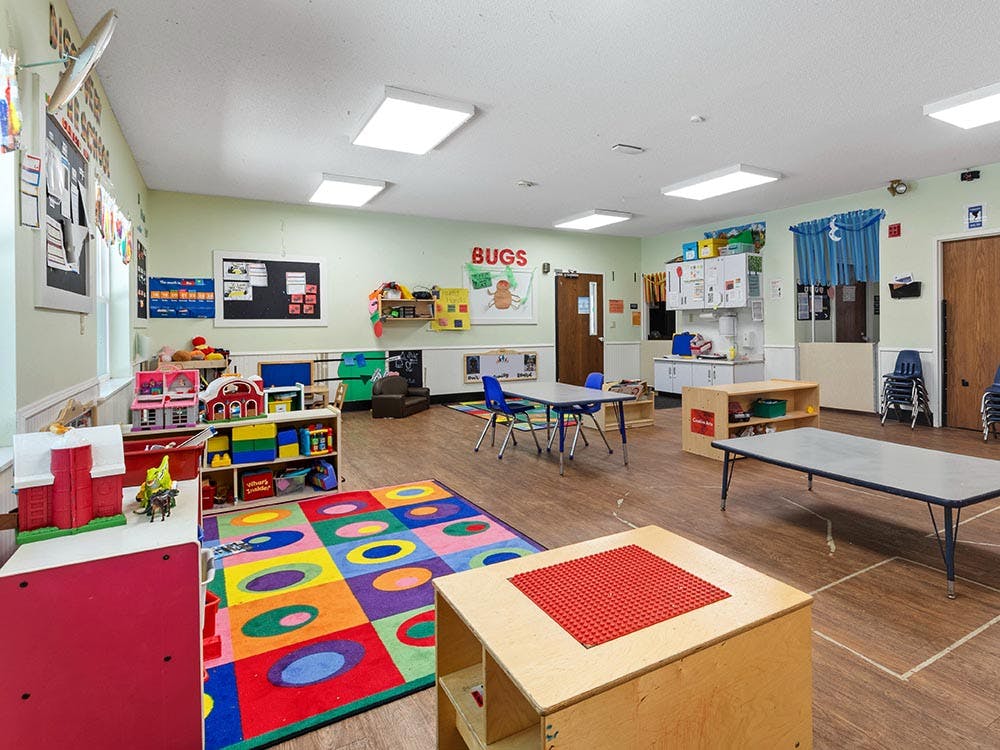 Classroom with colorful rug, play kitchen, and small tables