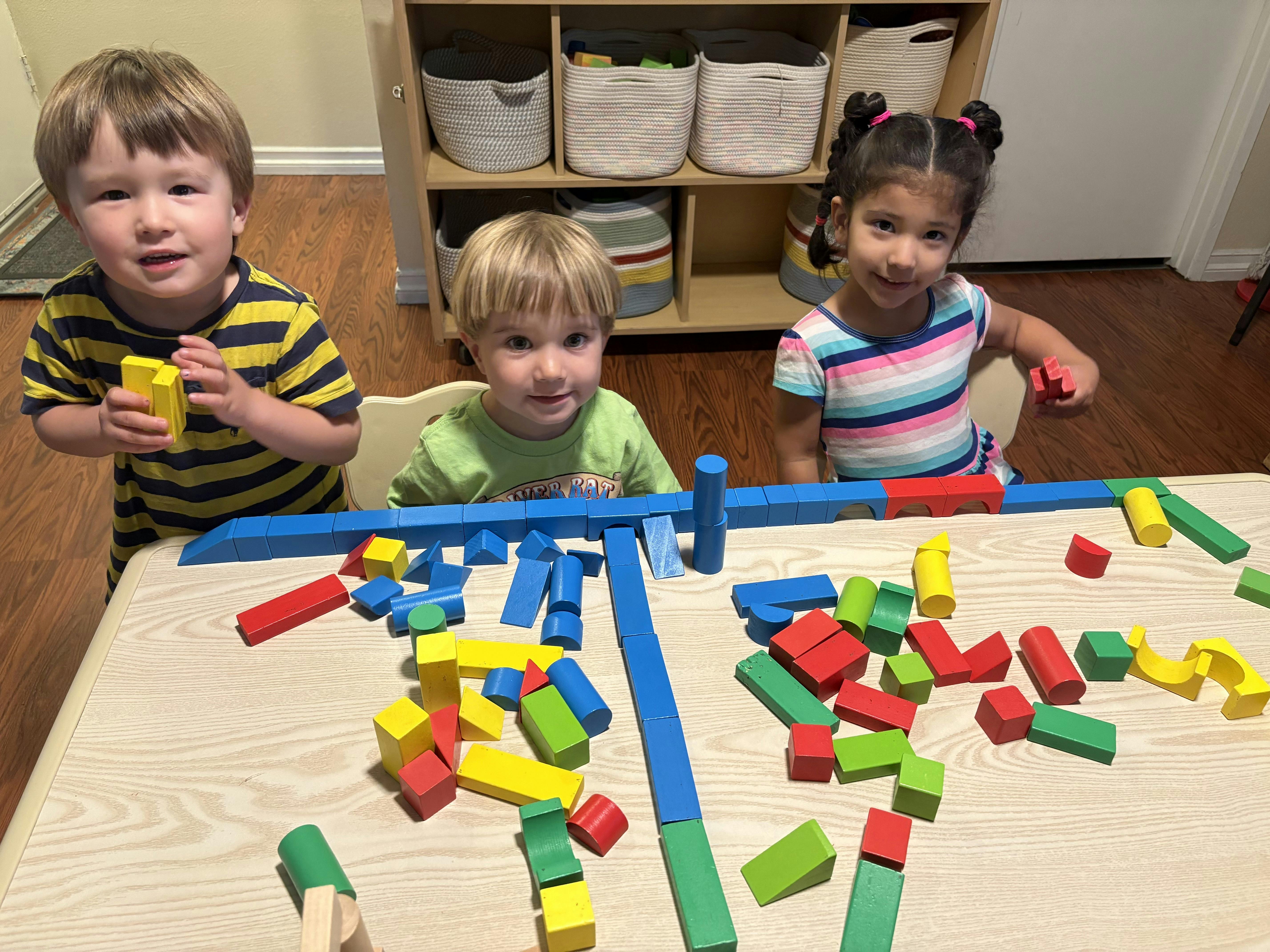 Three children playing with colorful building blocks at a table
