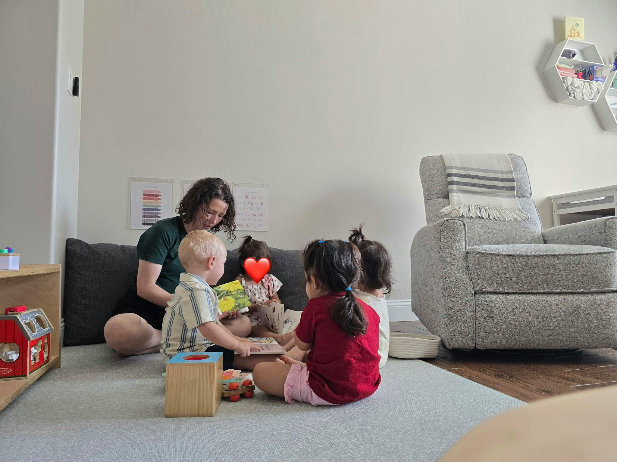 Adult sitting on the floor reading a book to a group of children