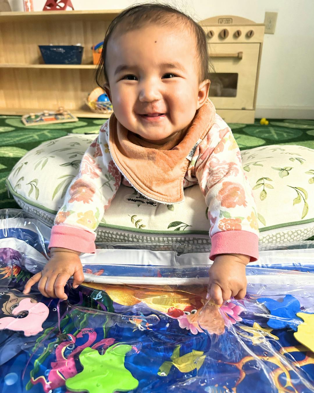 Smiling child on a cushion playing with a water mat