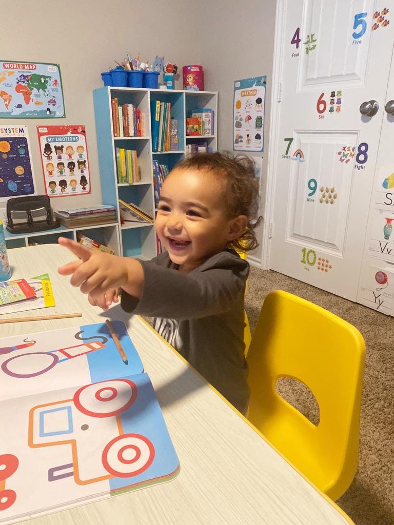 Child sitting at a table with a learning mat, pointing