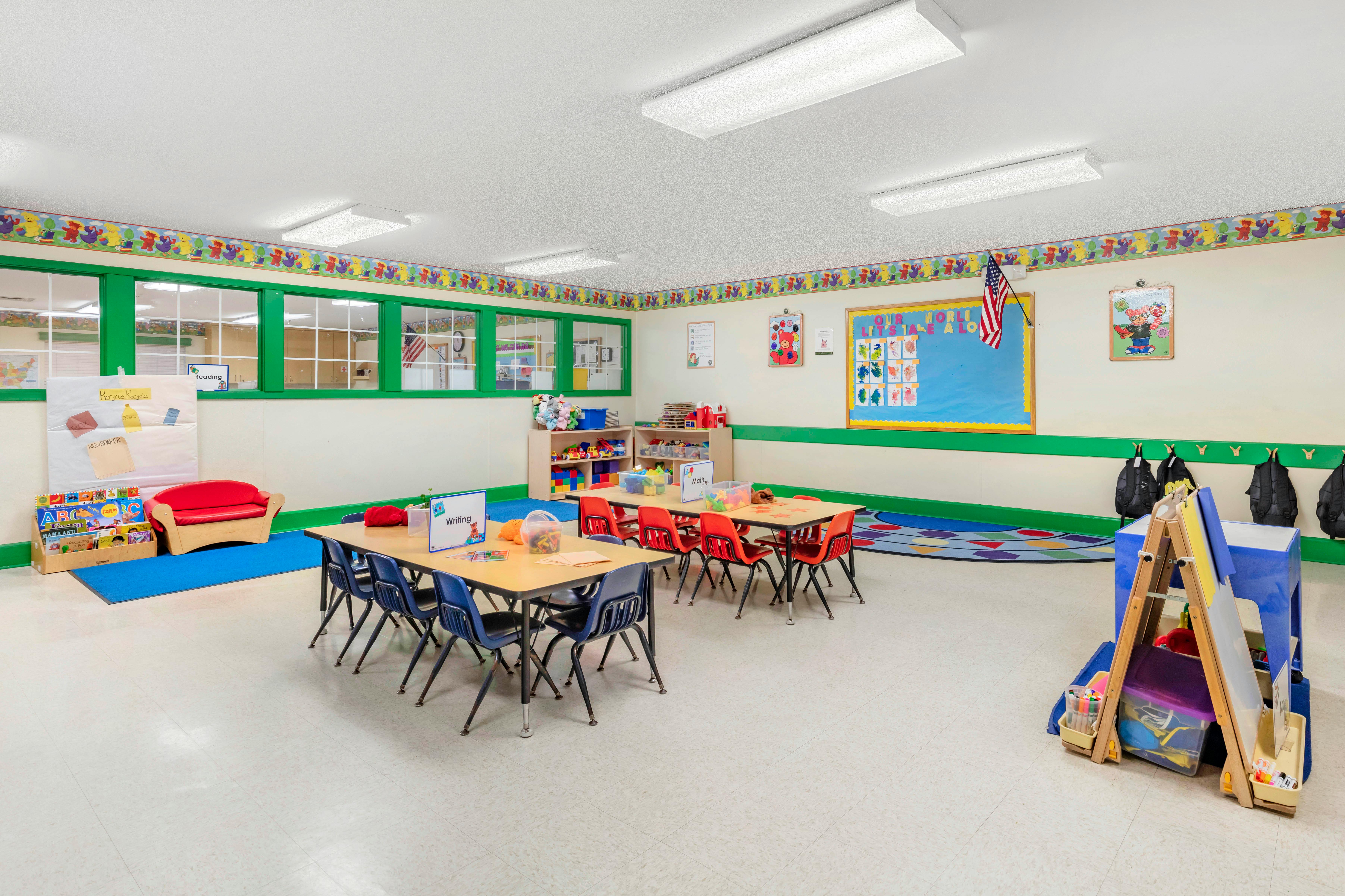Classroom with tables, chairs, bookshelves, play area, and activity boards