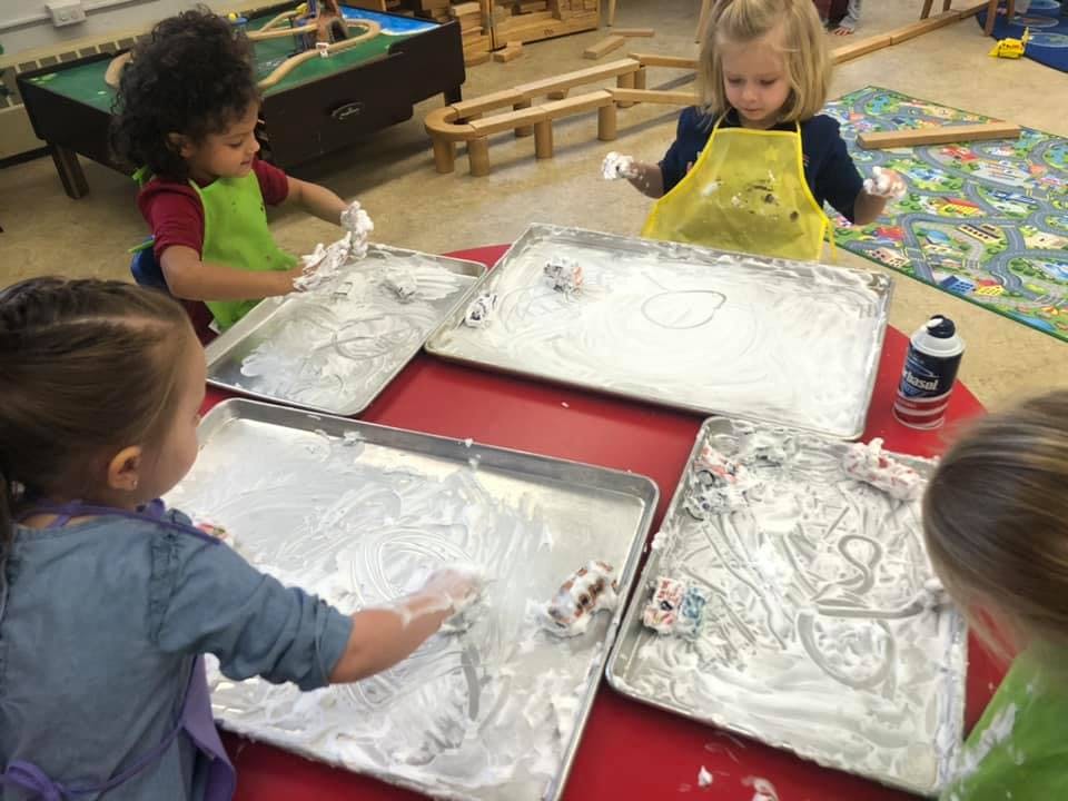 Children playing with shaving cream on trays