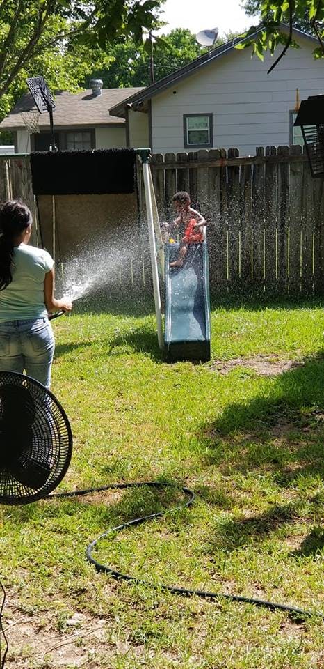 Person spraying water on a child on a slide in a backyard