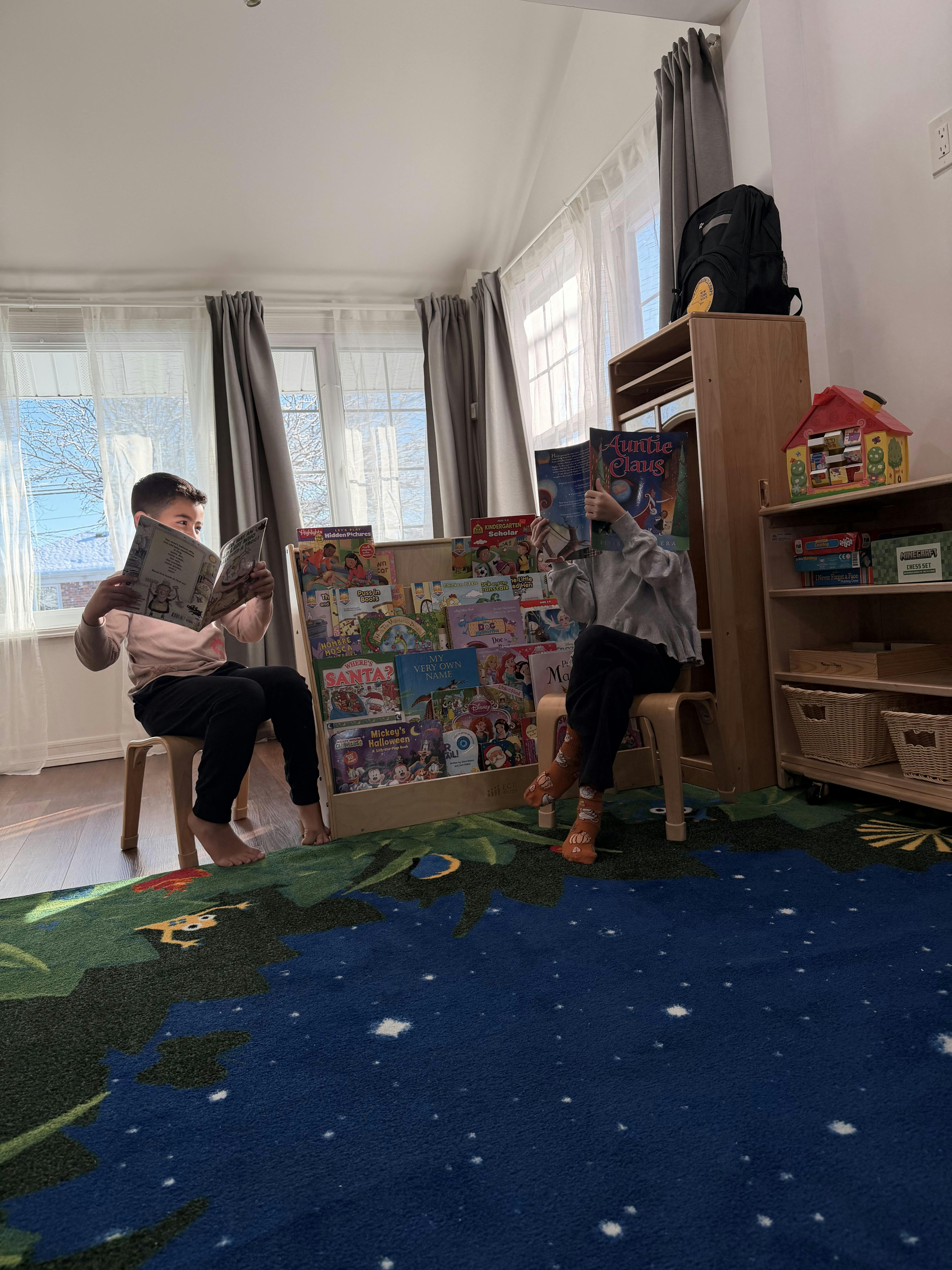 Two children sitting on stools reading books from a display shelf in a room