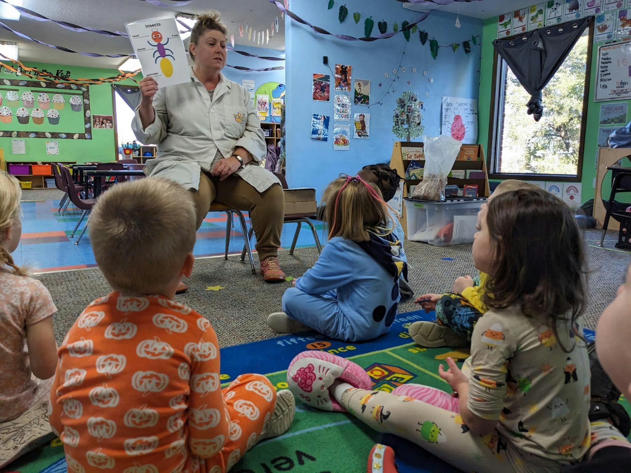 Adult showing an insects diagram to a group of children in a classroom