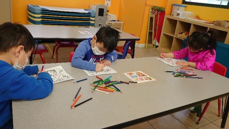 Three children coloring at a table in a classroom