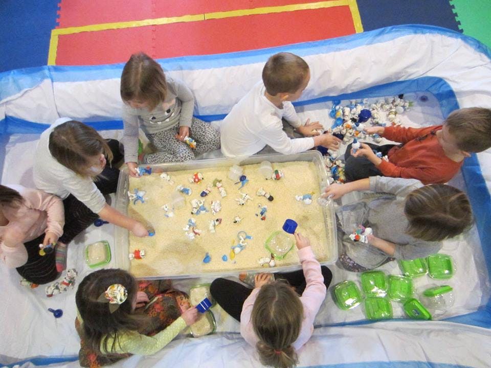 Children playing with a sensory bin filled with sand and small objects