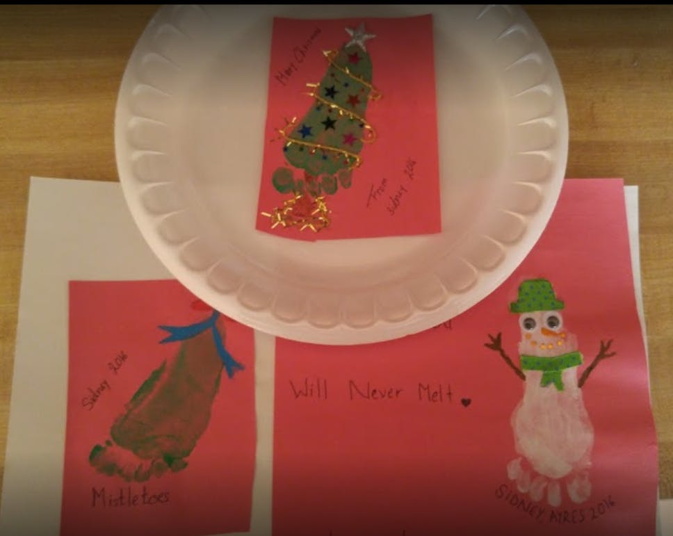 Three holiday-themed footprint crafts on red paper