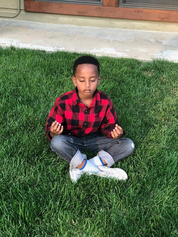 Child sitting cross-legged on grass with eyes closed