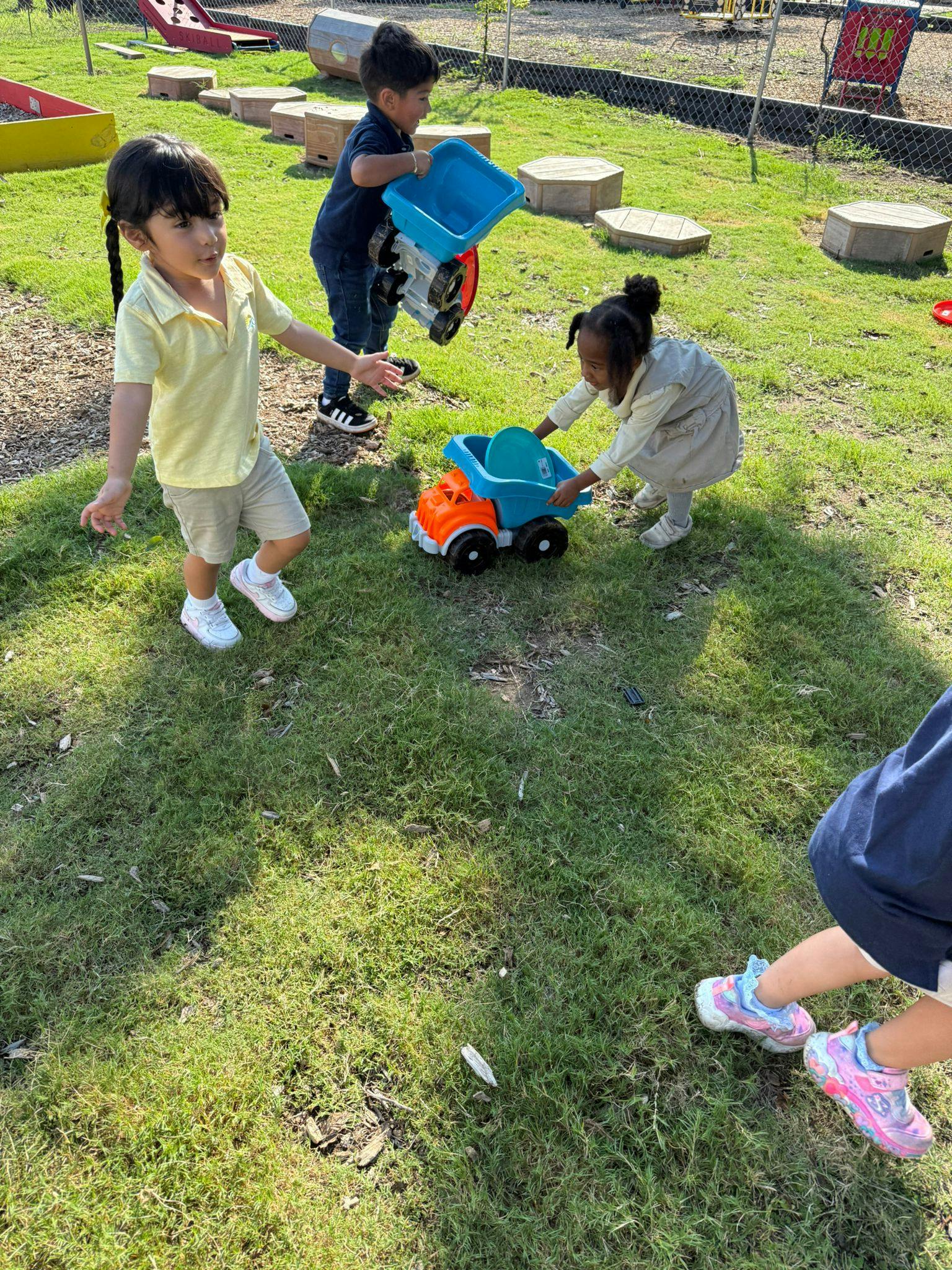 Three children playing with toy trucks on grass