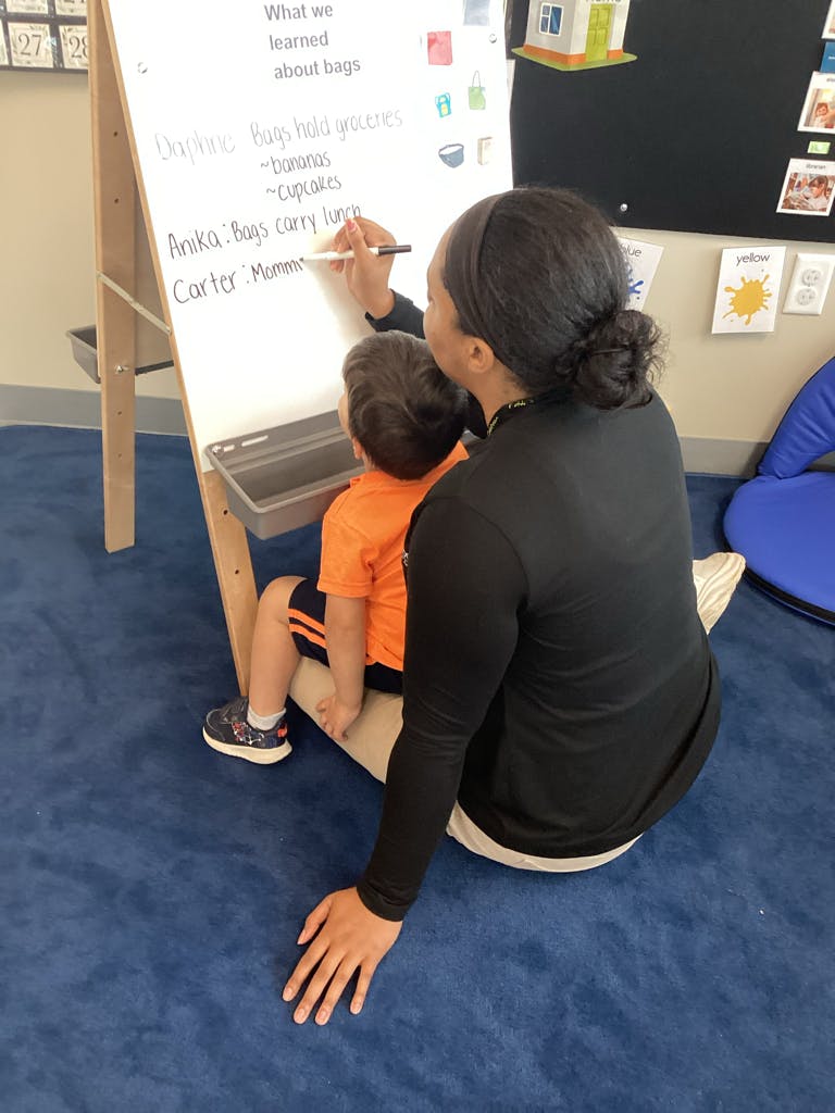 Person writing on a whiteboard with a child sitting in front