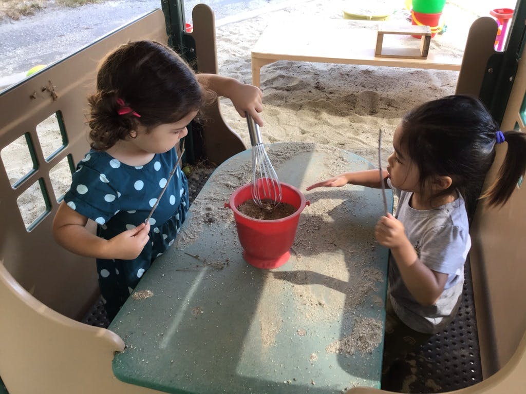 Two children playing with sand and kitchen utensils in a play structure