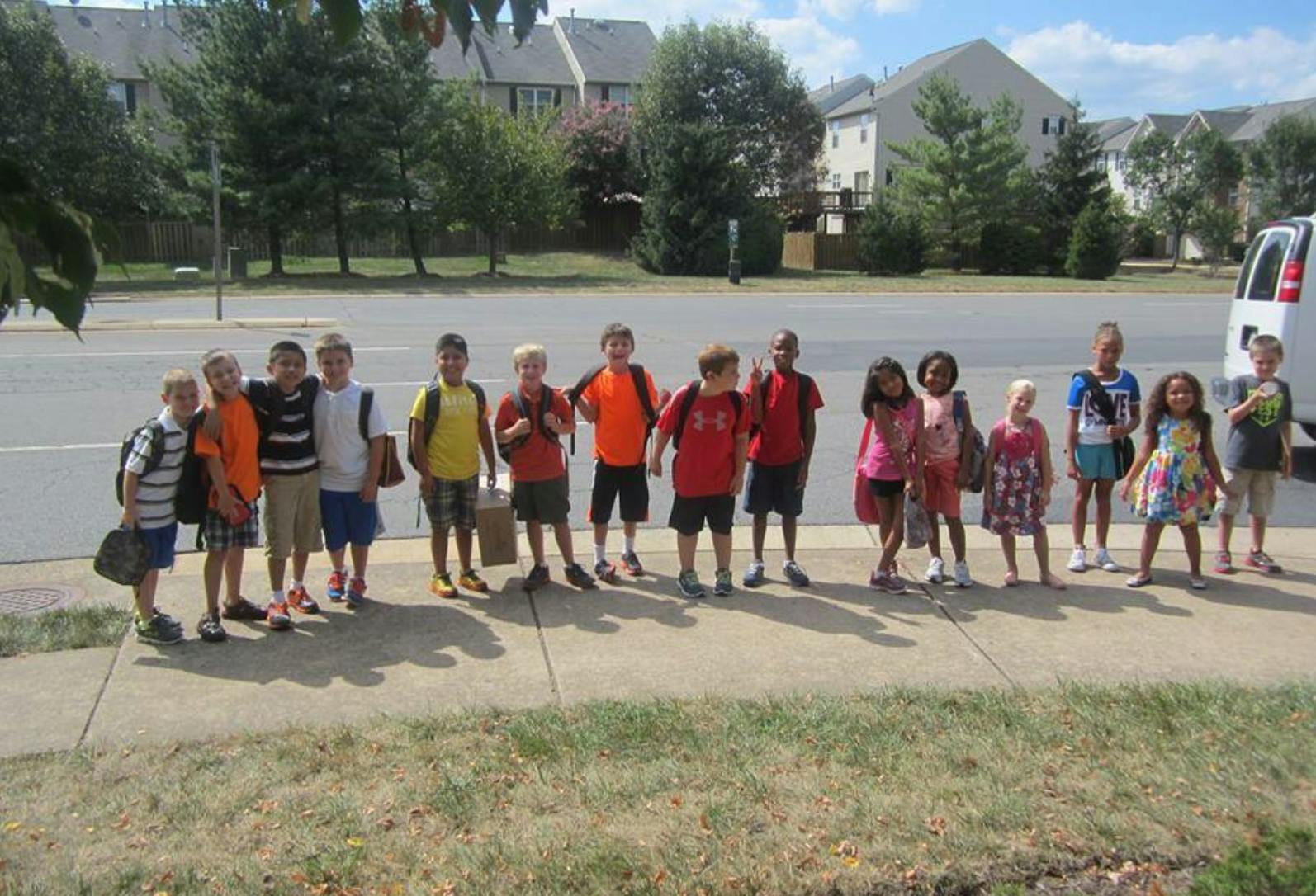 Group of children standing on a sidewalk next to a road