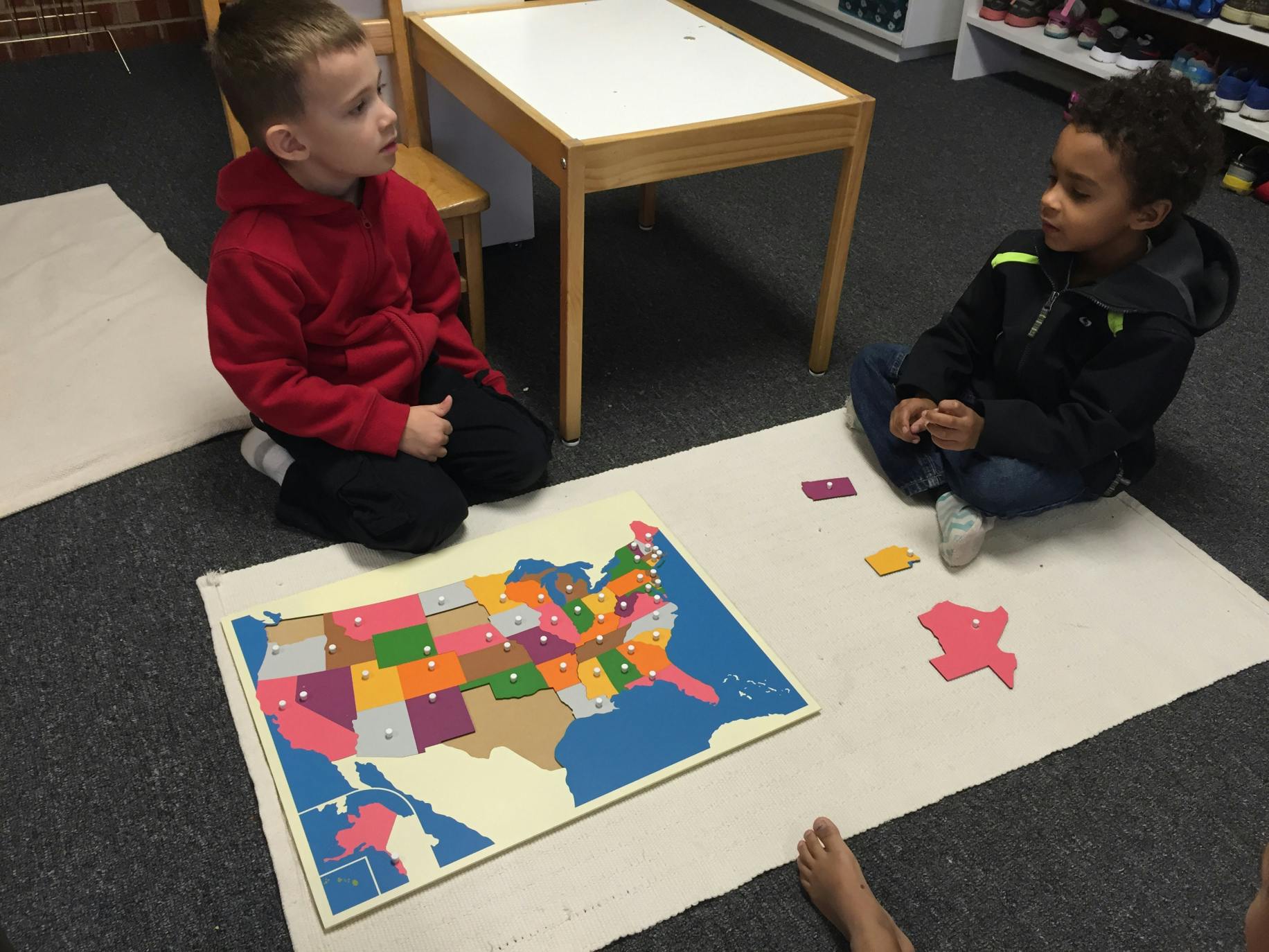 Two children sitting on the floor with a US map puzzle