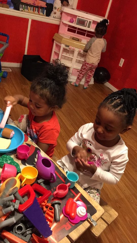 Two children playing with toys at a table, one child at a play kitchen