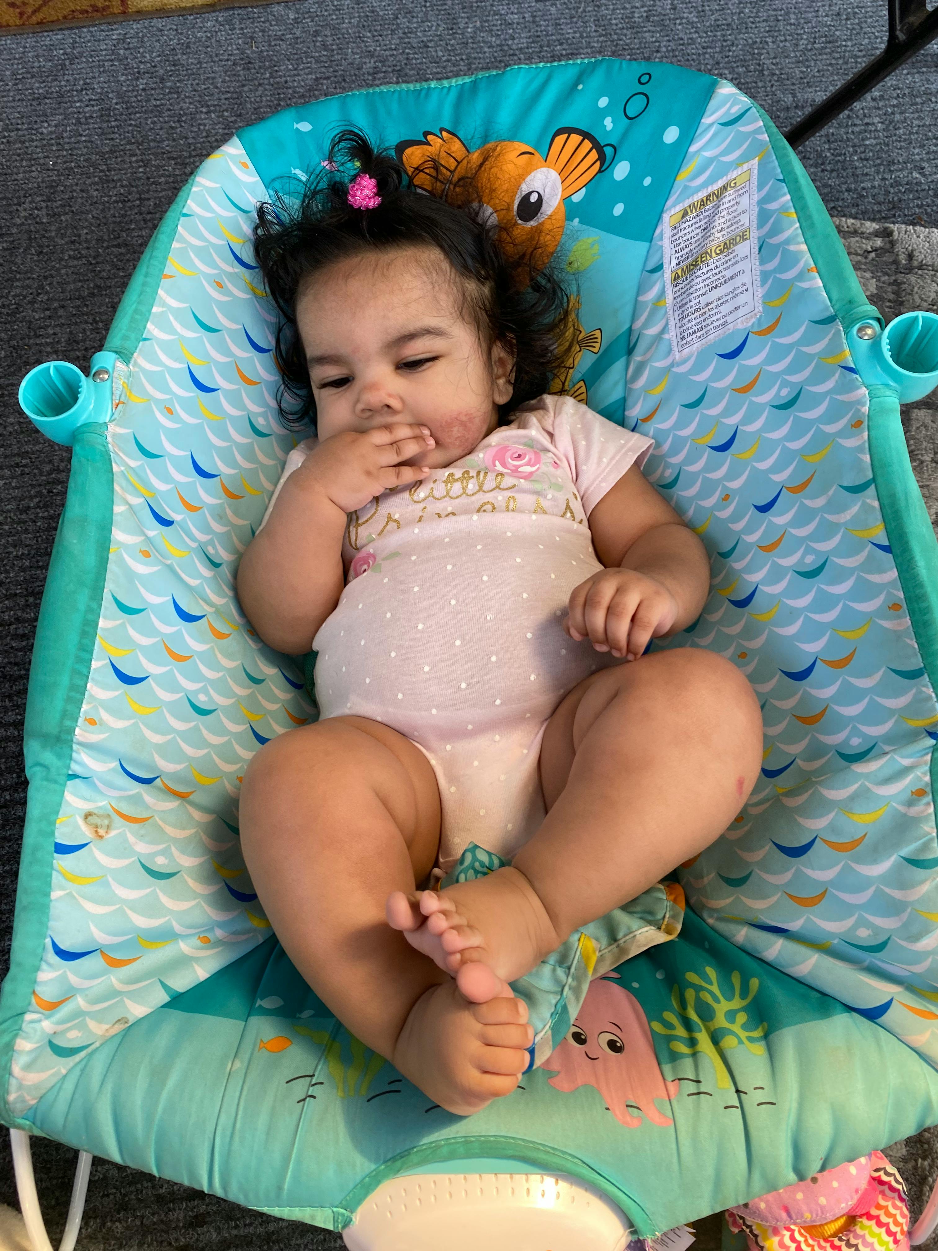Child lying in a baby bouncer with hand near mouth
