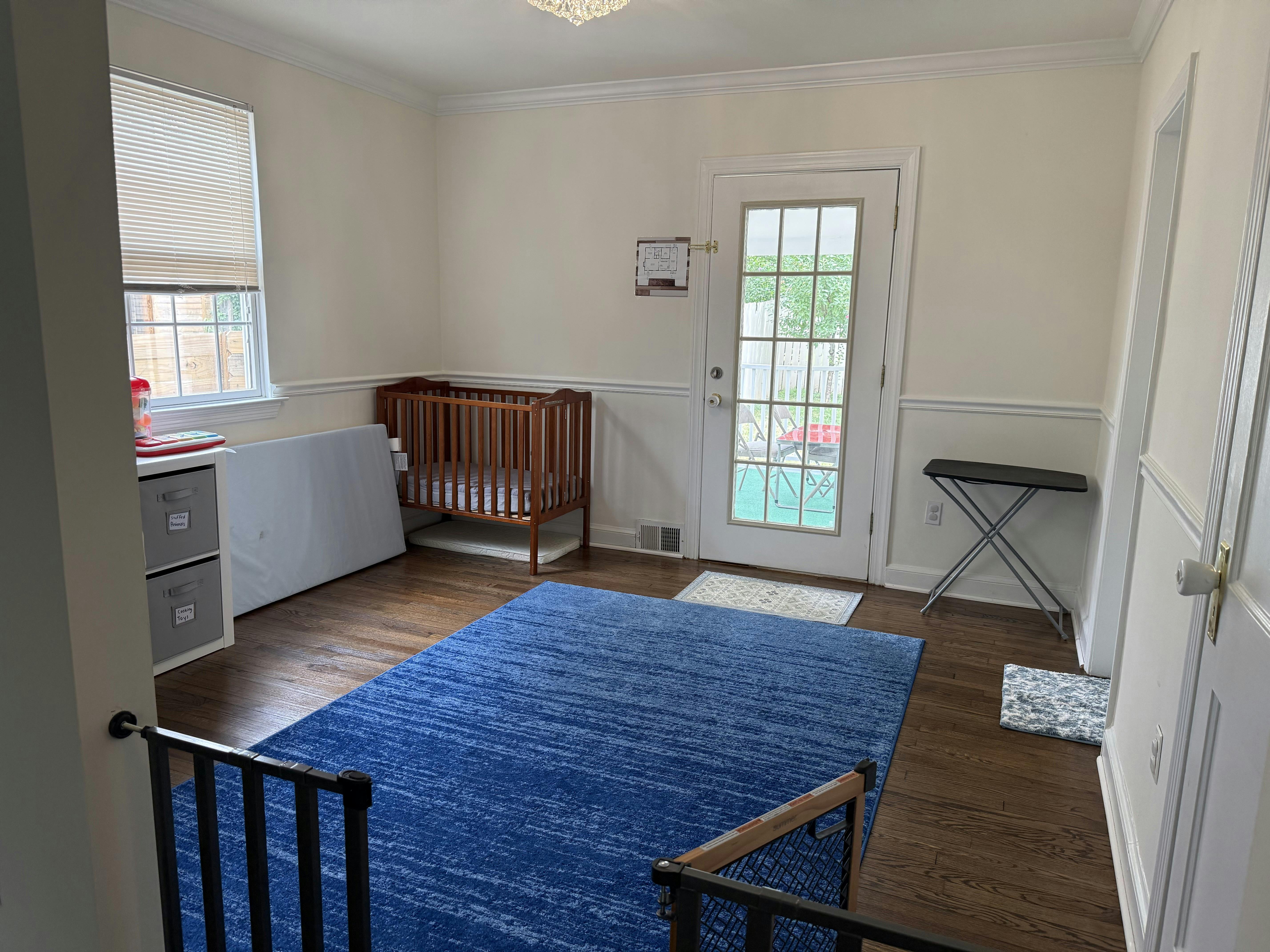 Crib and blue rug in a sunlit room with a doorway
