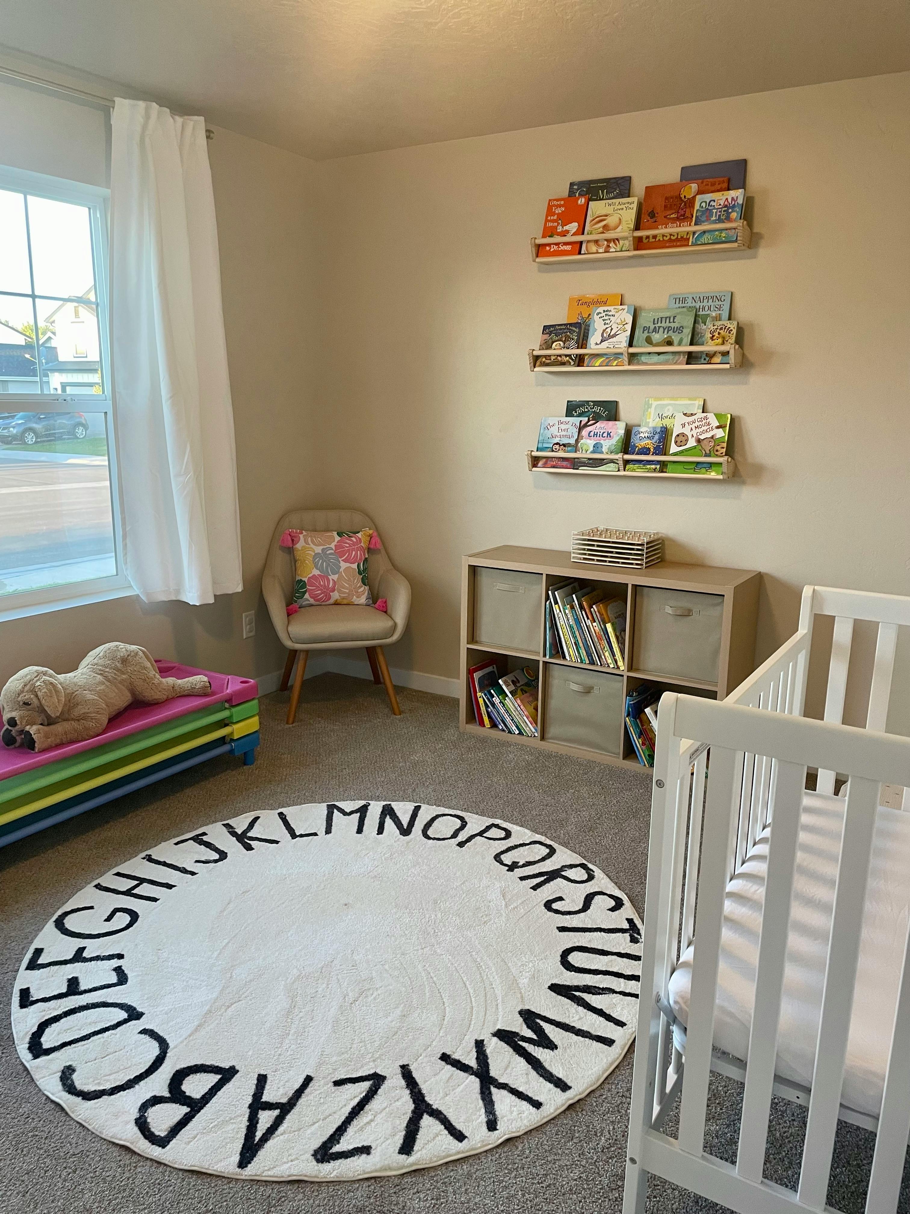 Nursery room with a white crib, alphabet rug, and bookshelves