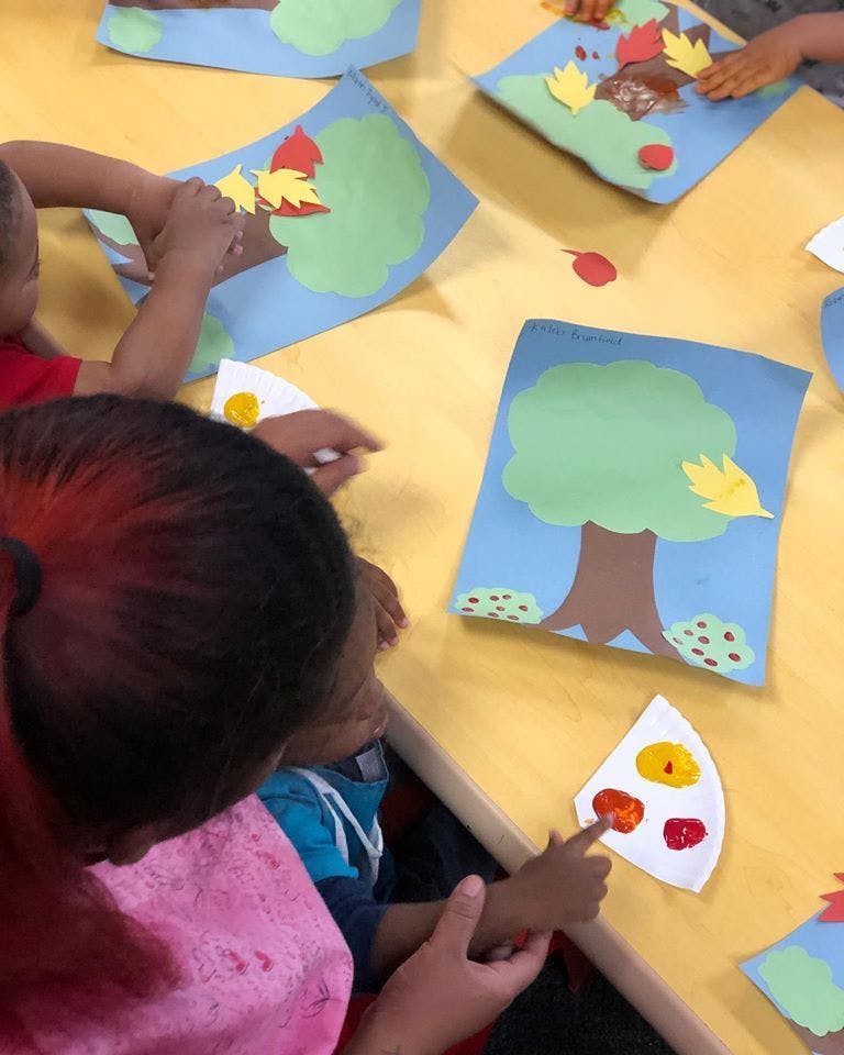People doing crafts with paper trees and leaves in a classroom