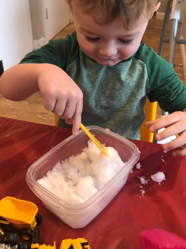 Child playing with snow in a container using a yellow spoon