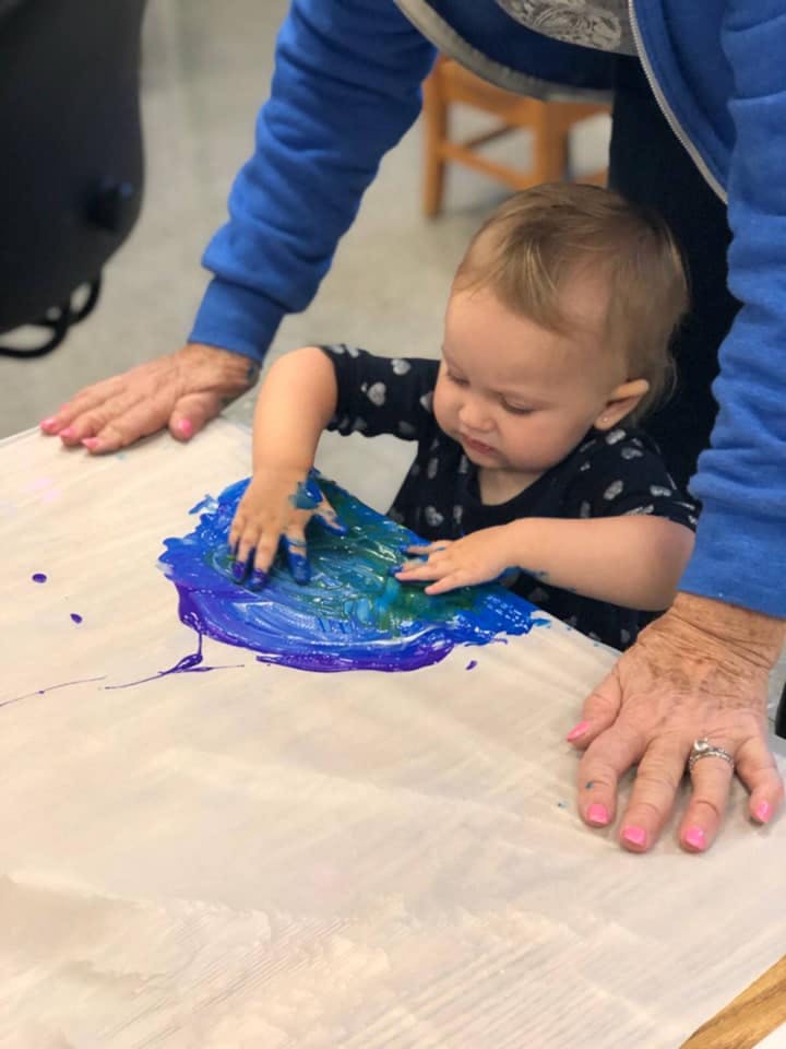 Child and person finger painting with blue and purple paint