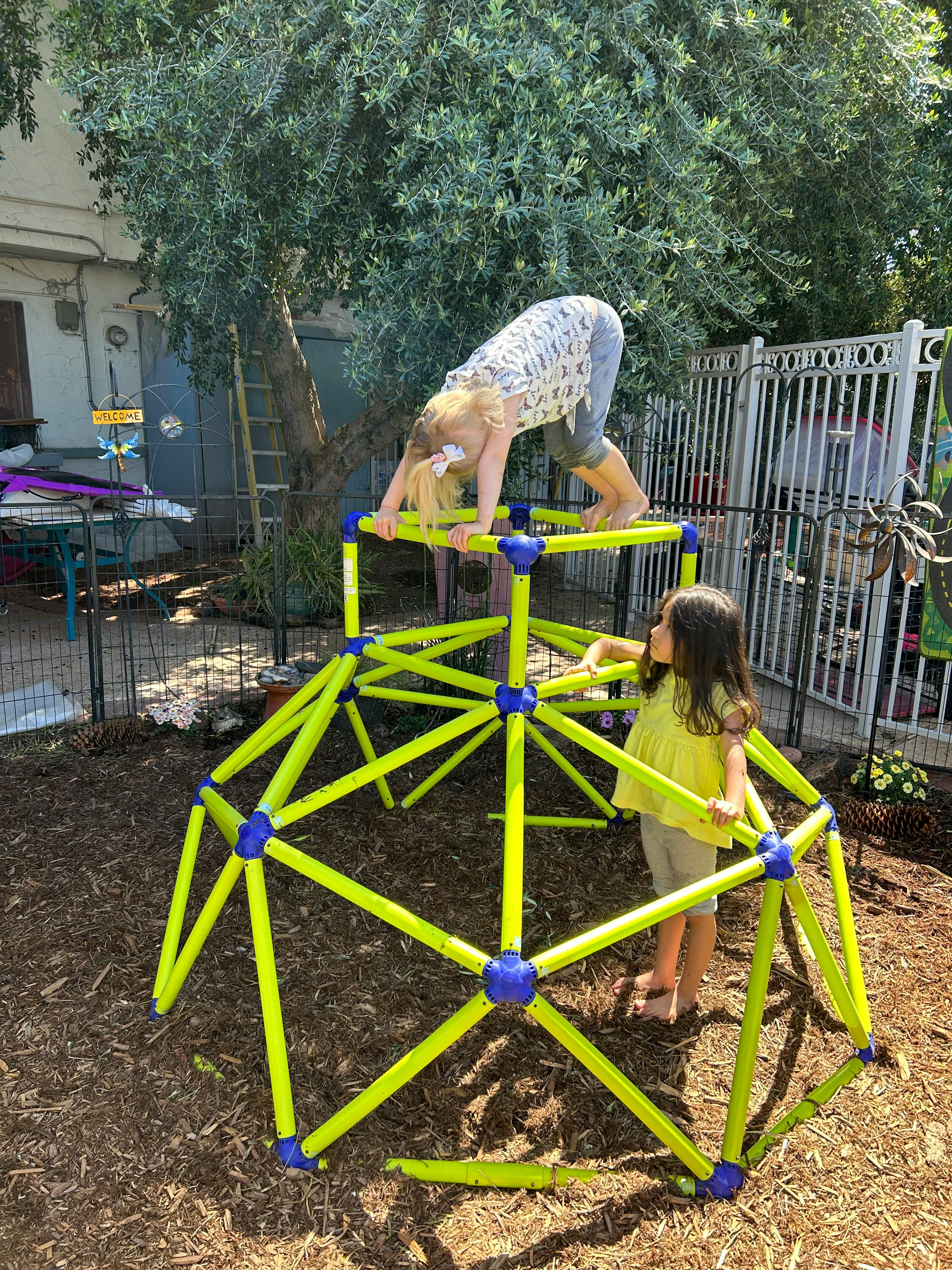 Two children playing on a green climbing dome