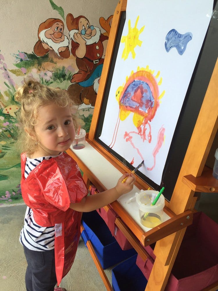 Child in a red smock painting at an easel