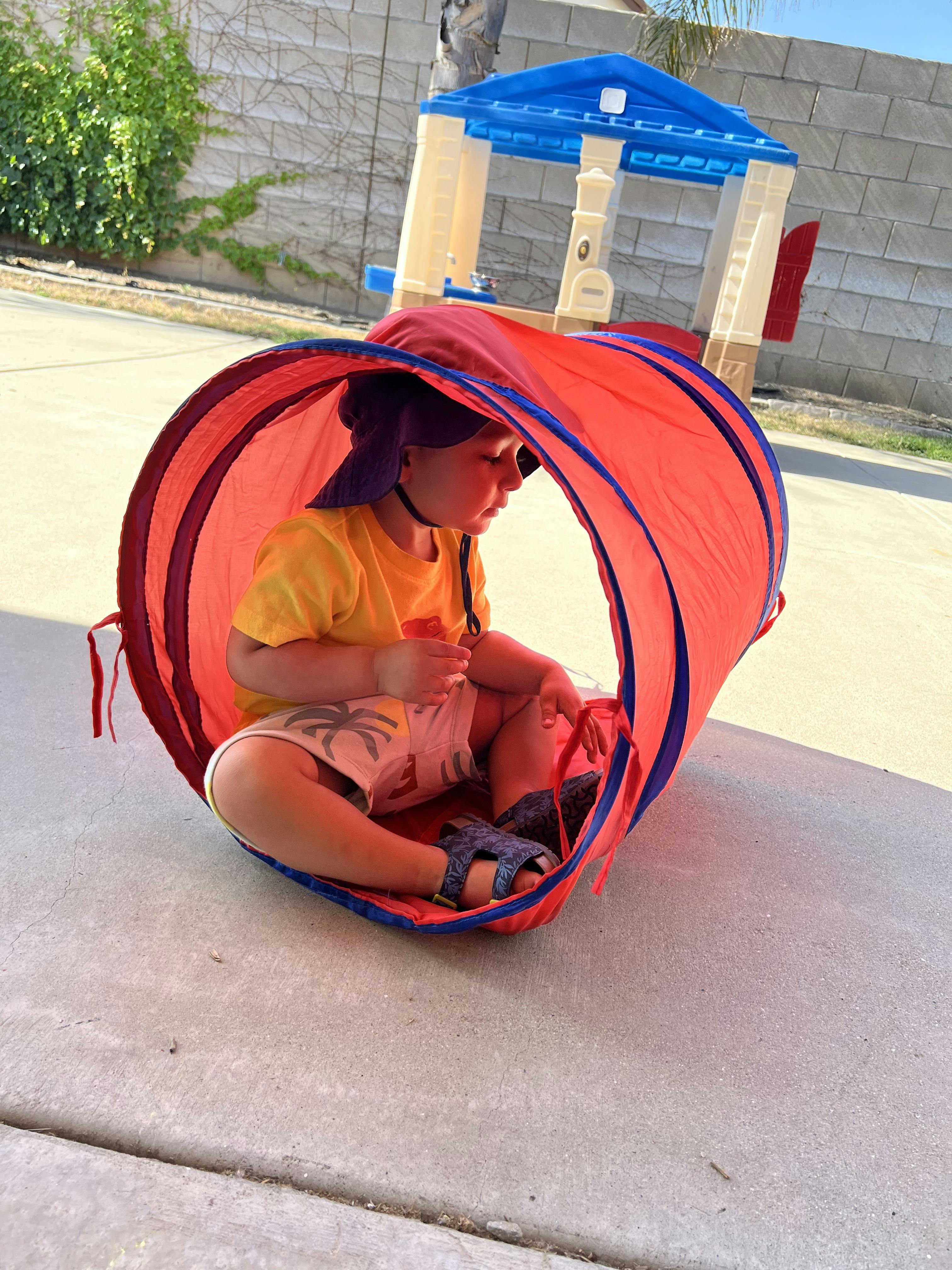 Child sitting inside a red play tunnel