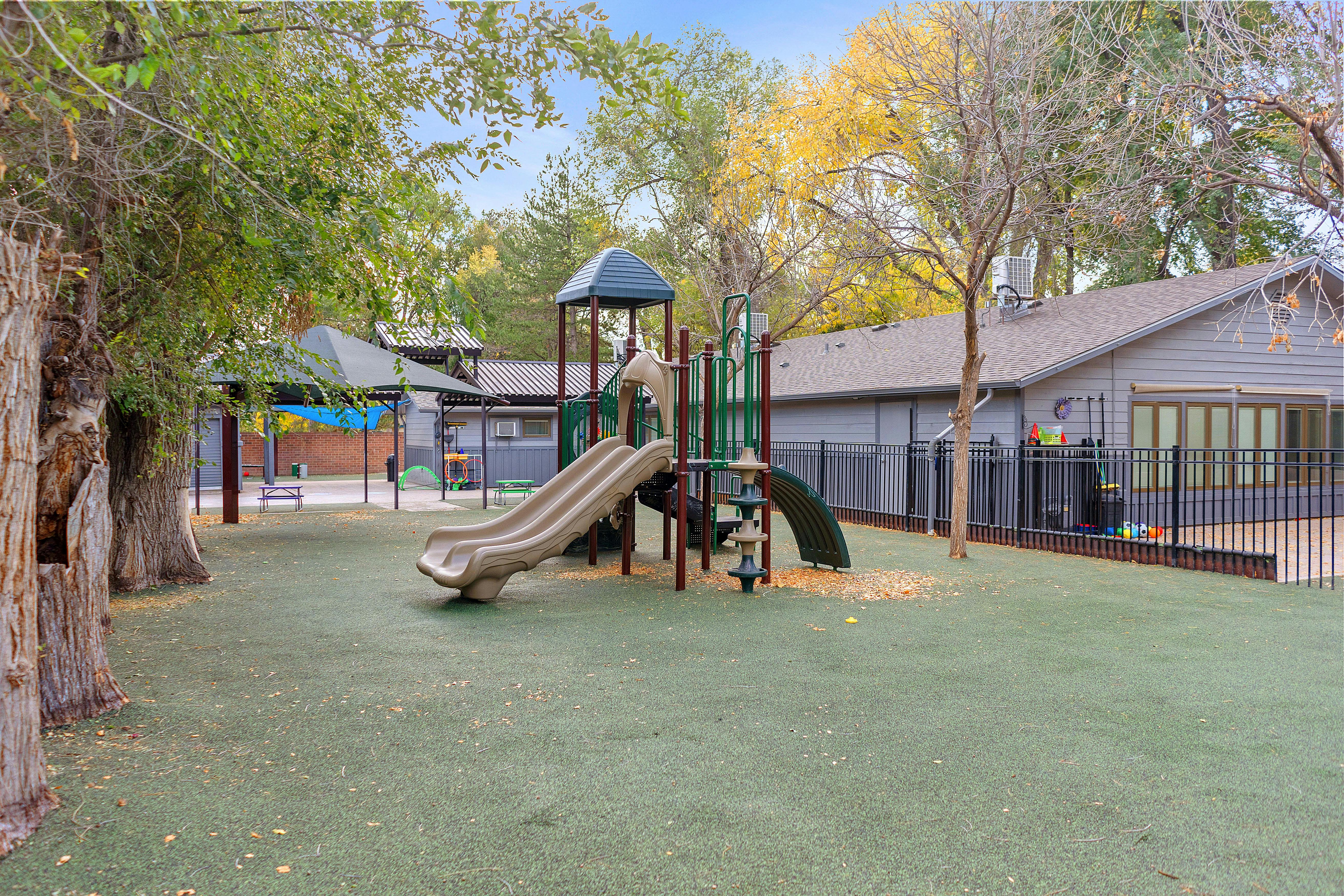 A playground with a slide structure and swings, surrounded by trees