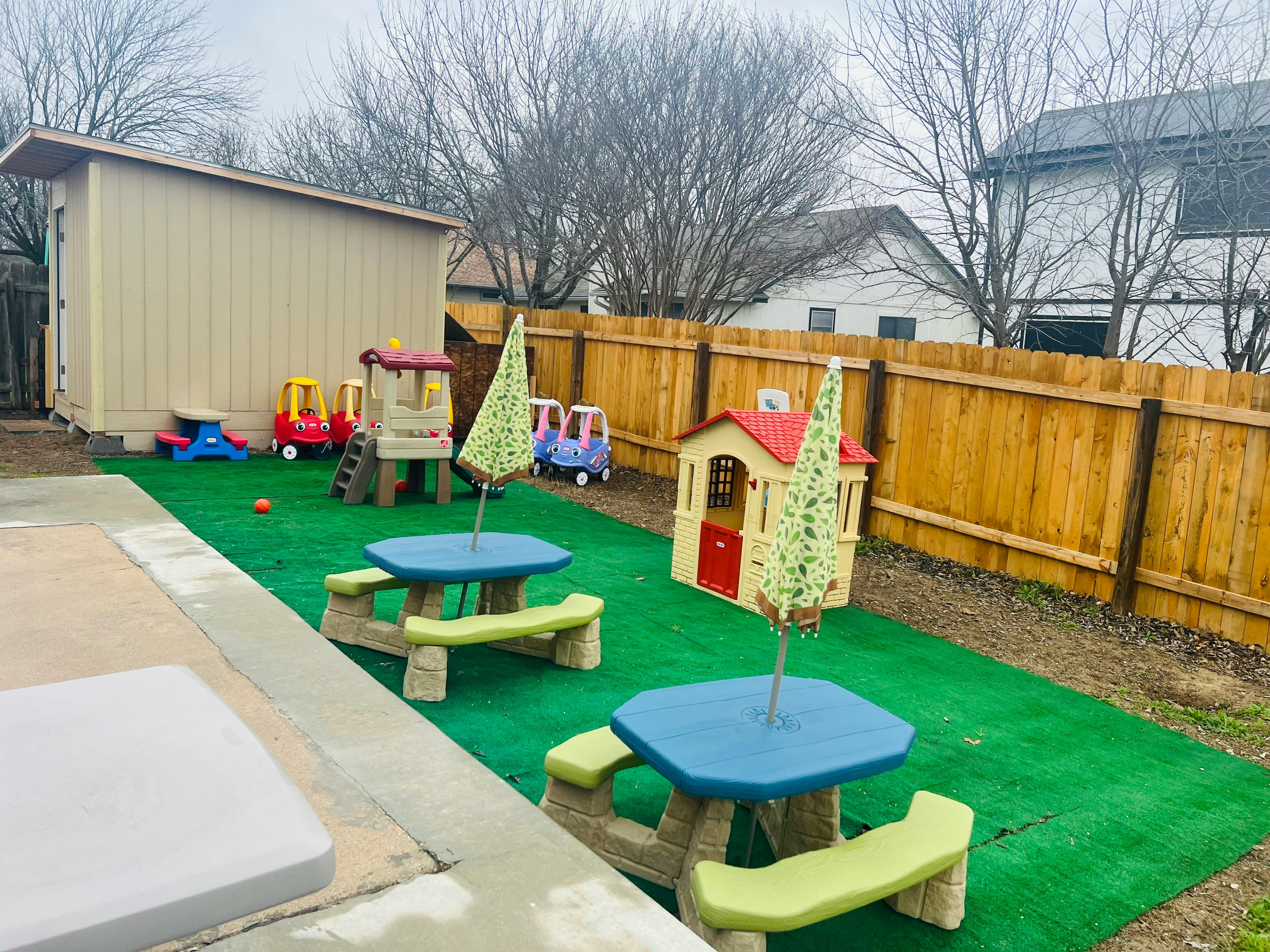 Outdoor play area with artificial grass, picnic tables, and playhouses