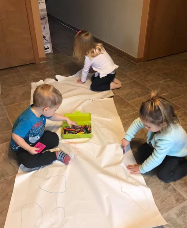 Three children drawing on a large sheet of paper on the floor