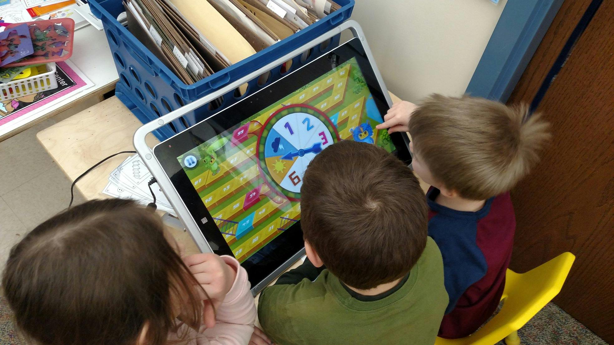 Children looking at a tablet with a clock game on the screen
