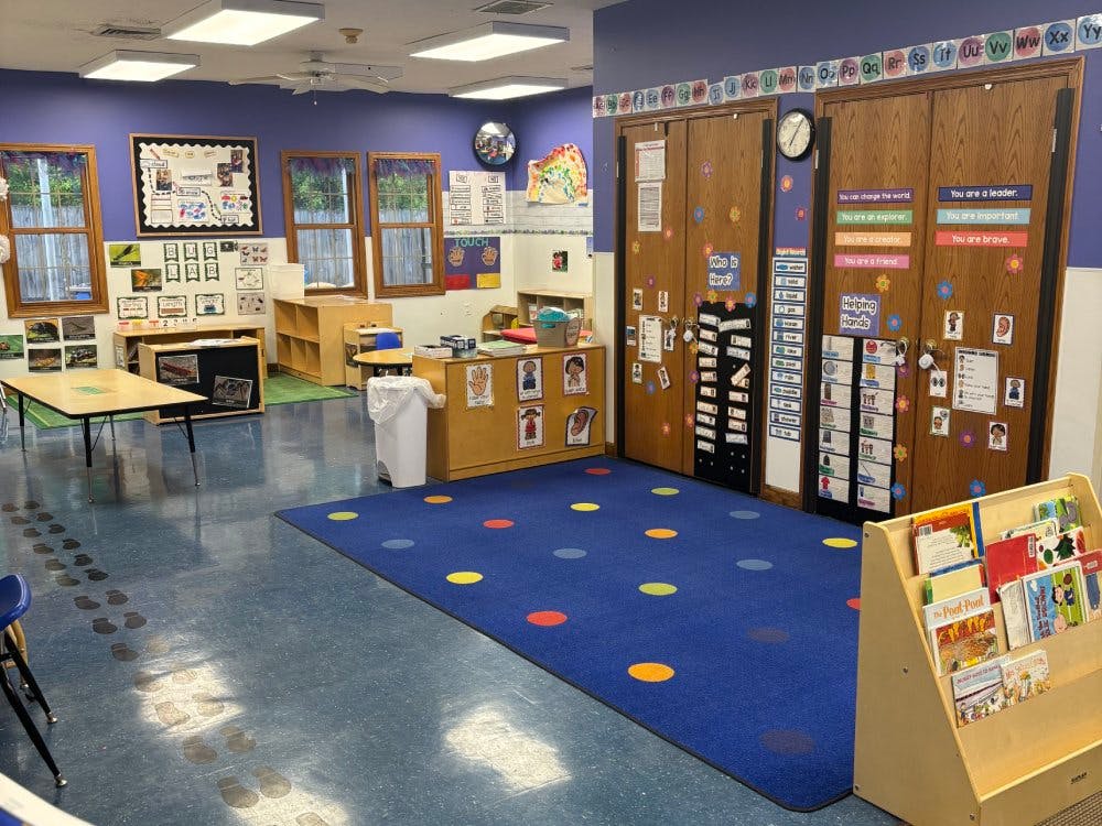 Empty classroom with colorful rug, tables, and cabinets