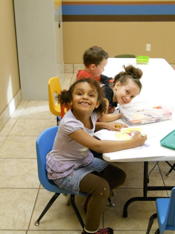 Three children sitting at a table, one child coloring