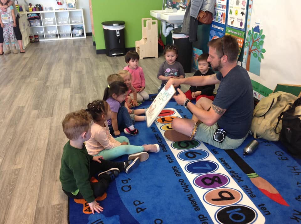 Adult reading a book to a group of children sitting on a rug