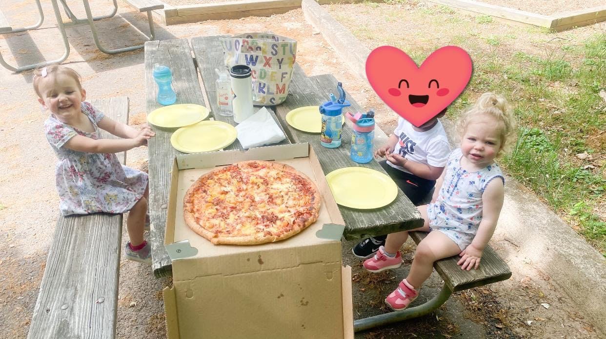 Three children sitting at a picnic table with a pizza