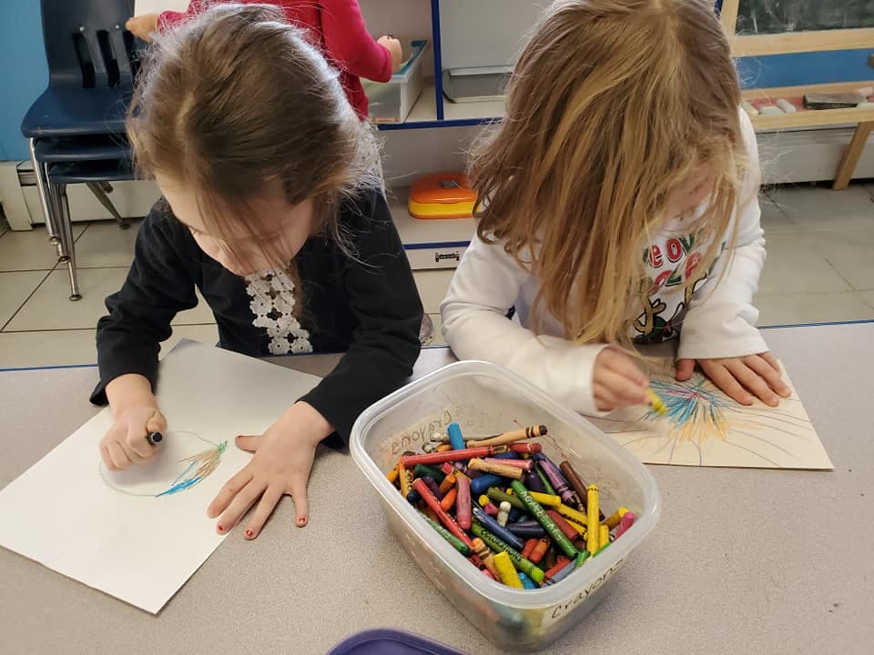 Two children drawing with crayons at a table