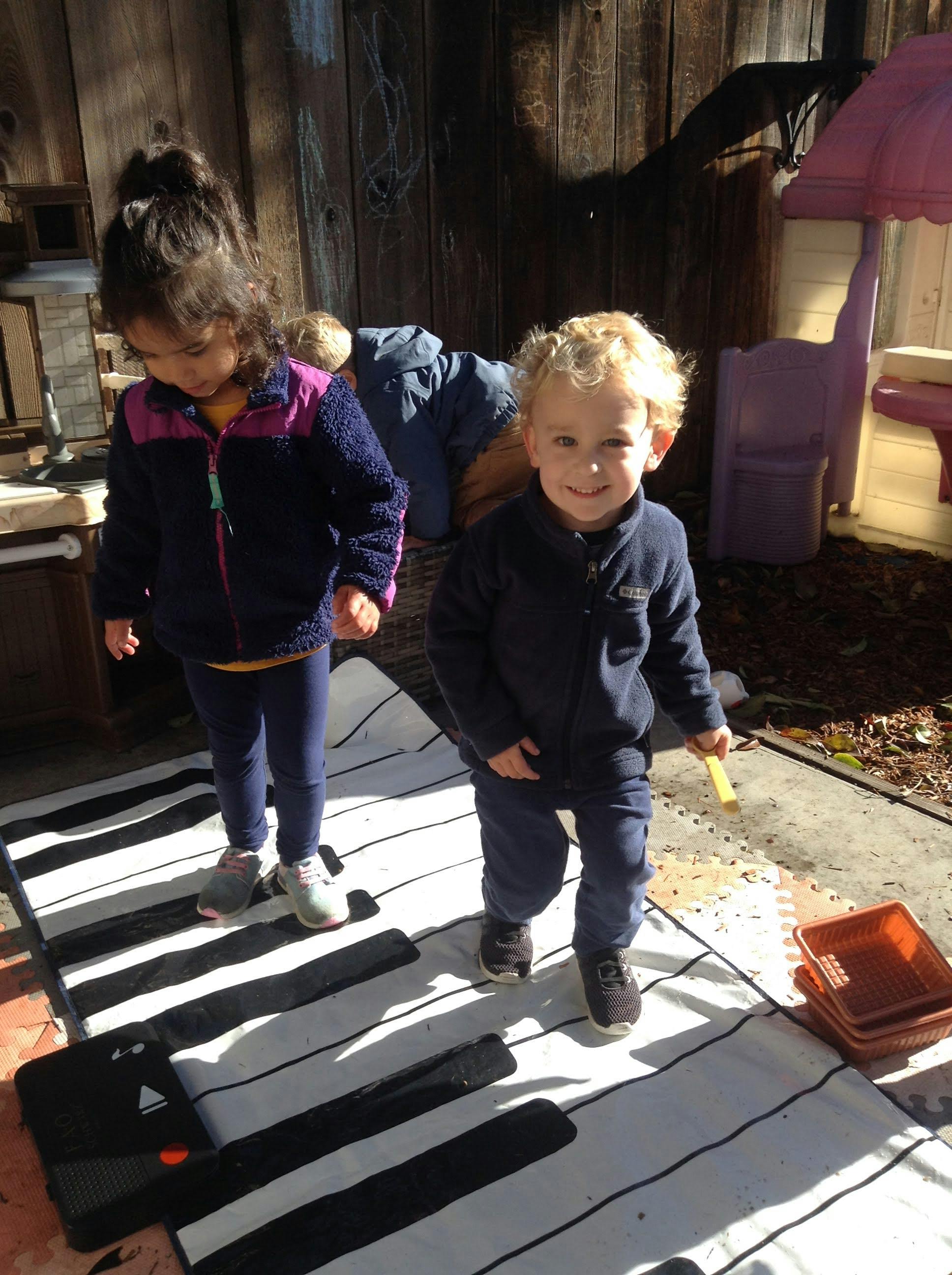 Two children standing on a piano mat outdoors