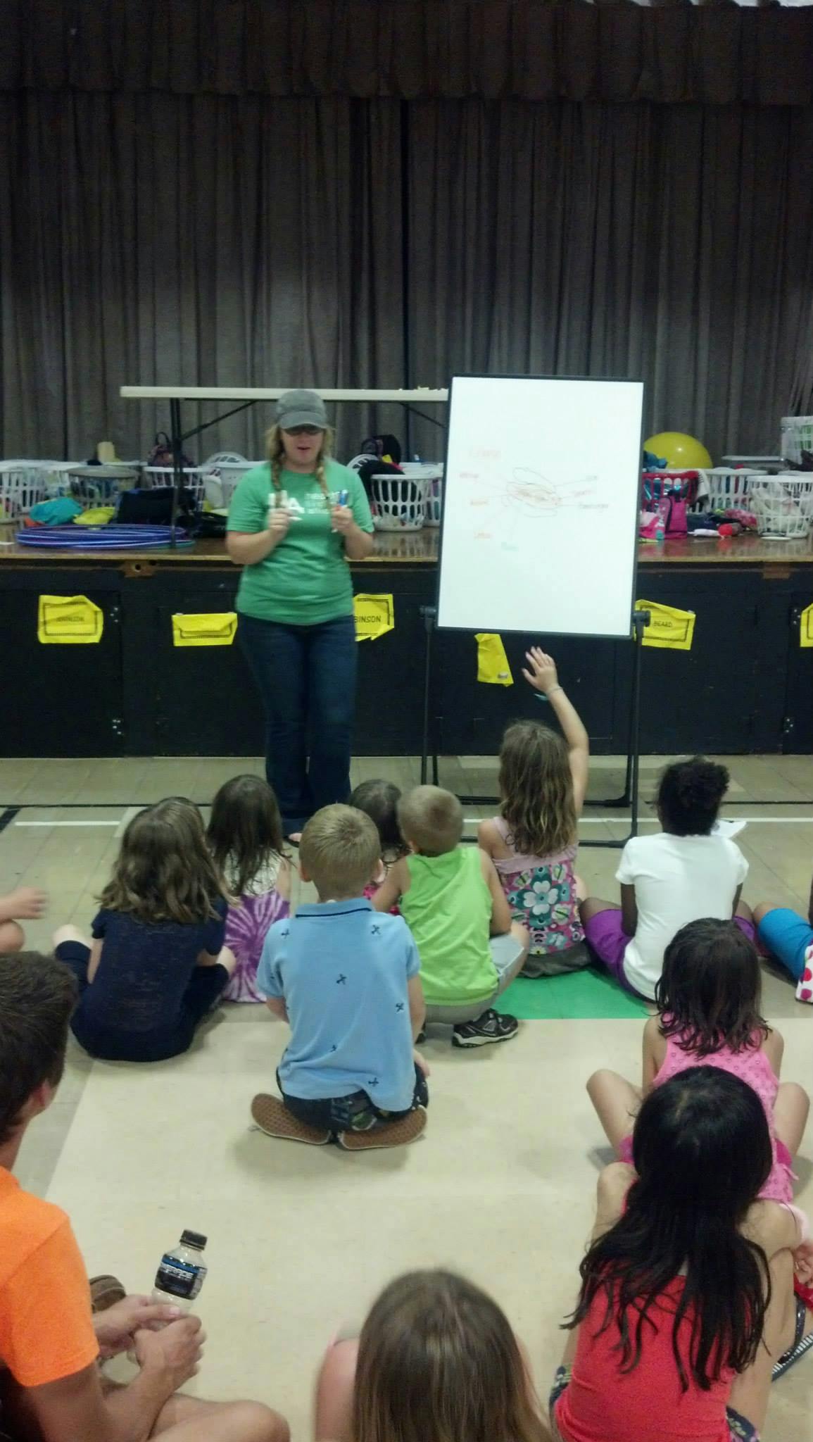 Person teaching children sitting on the floor, one child raising a hand